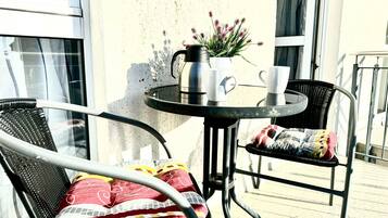 Ein Balkon mit rundem Tisch, zwei Stühlen, einem Blumentopf und einem Wasserkocher.
