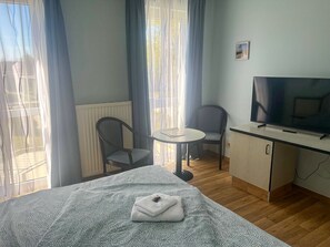 Ein Hotelzimmer mit Bett, Fernseher, kleinem Tisch, zwei Stühlen und einem fensterbepflanzten Fenster.