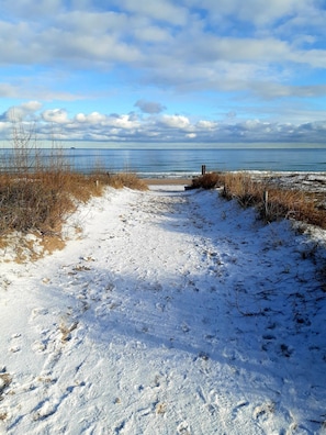 Un sentier enneigé qui mène à une plage d’où l’on a une vue dégagée sur l’océan et un ciel nuageux.
