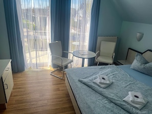 A hotel room with a bed, two chairs, a small table, and a view through sheer curtains. - Double Room 35 - Mönchgut Beach House Bed & Breakfast, Lobbe (Mönchgut)