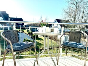 Un balcon avec deux fauteuils en osier, une petite table et une rambarde en métal.
