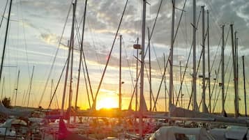 Ein Yachthafen mit mehreren Segelbooten, ein klarer Himmel und ein Sonnenuntergang im Hintergrund.