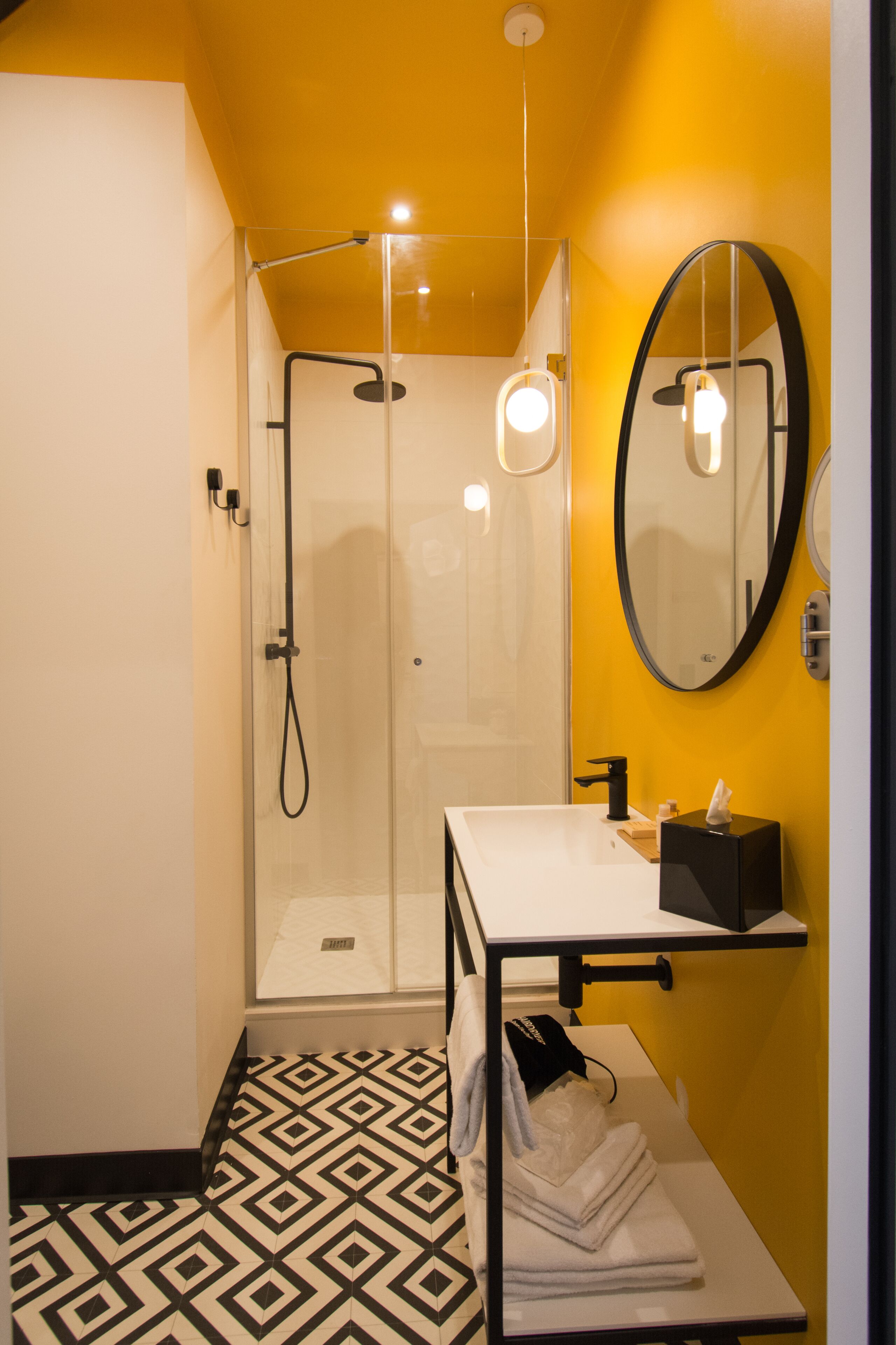 Un baño moderno con ducha de vidrio, un lavamanos blanco, un perchero negro y un espejo con marco negro.
