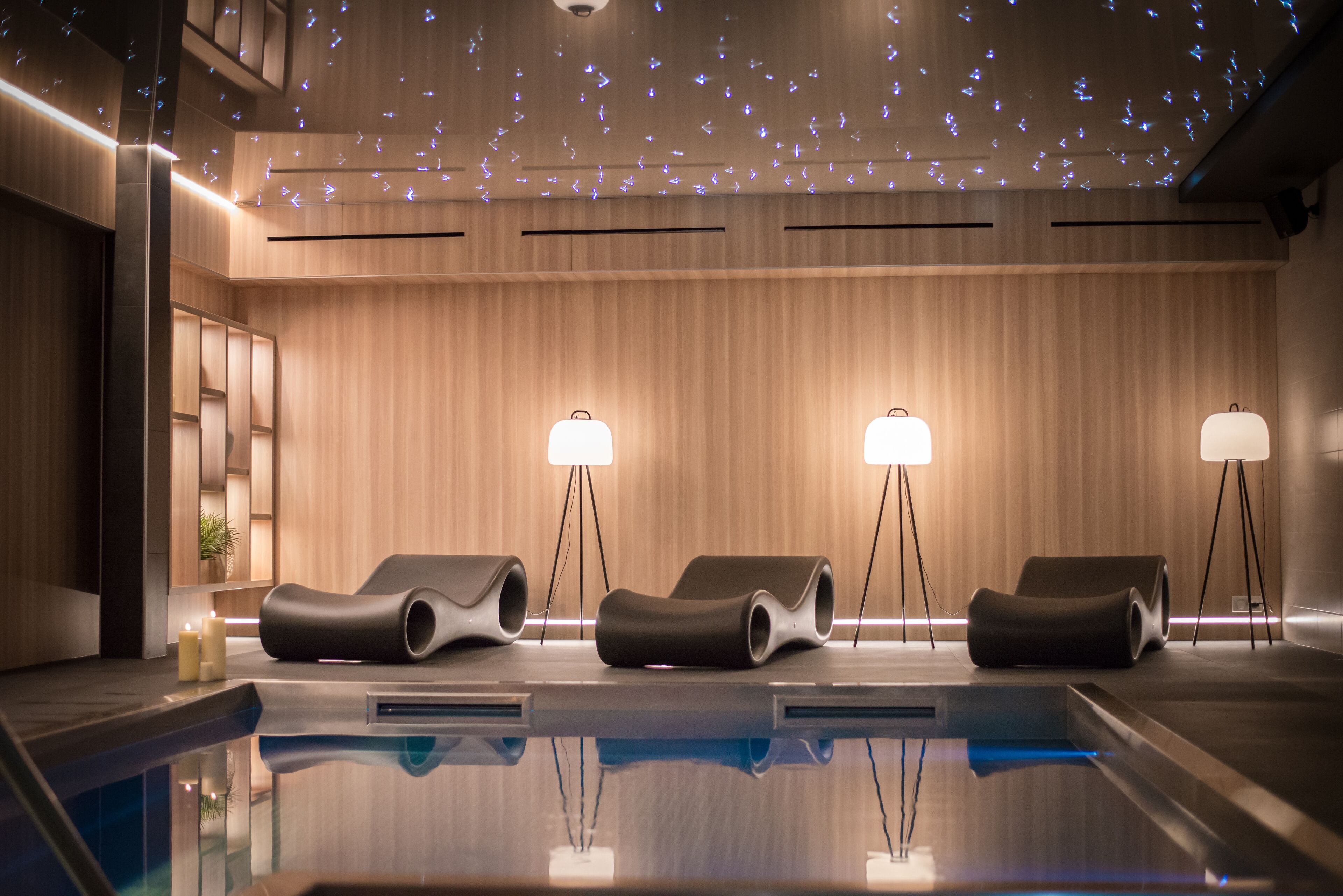 Un espace spa moderne doté d’une piscine, de murs recouverts de panneaux en bois et de trois fauteuils de relaxation.