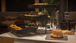 A buffet setup with various pastries and bread on wicker stands, a bundt cake on a cutting board, and a toaster on the counter. - L'Hôtel & Spa  Ribeauvillé (Ribeauvillé)