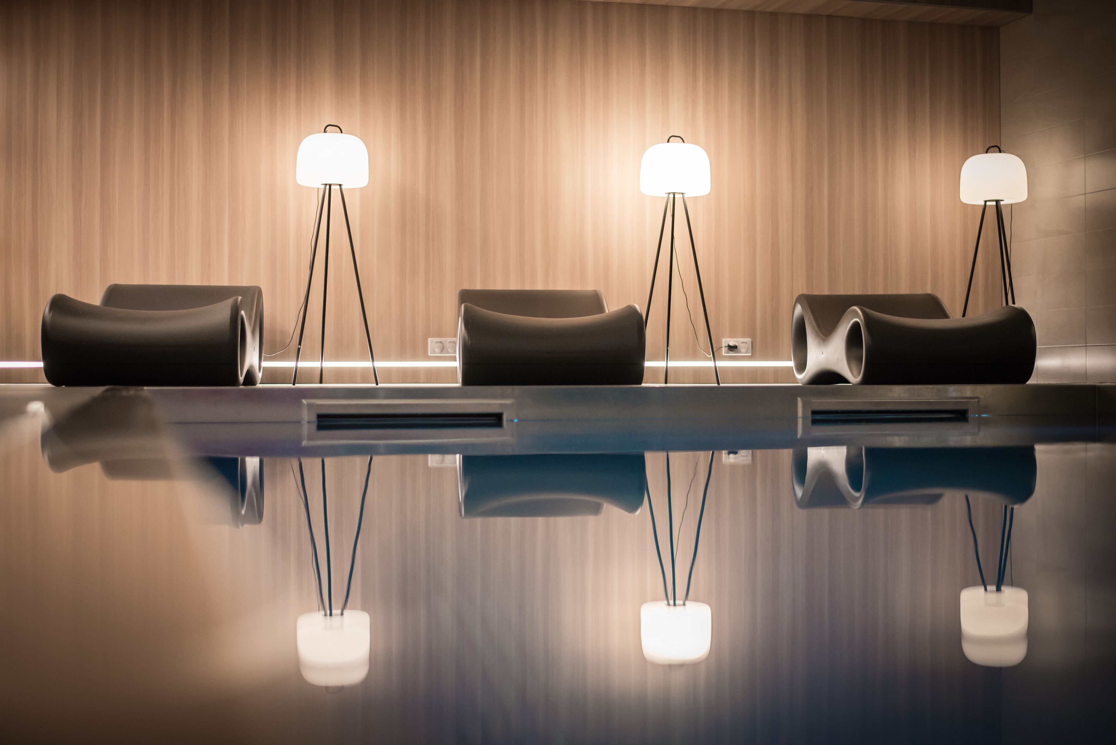 A reception area with three black chairs and three floor lamps with white shades.