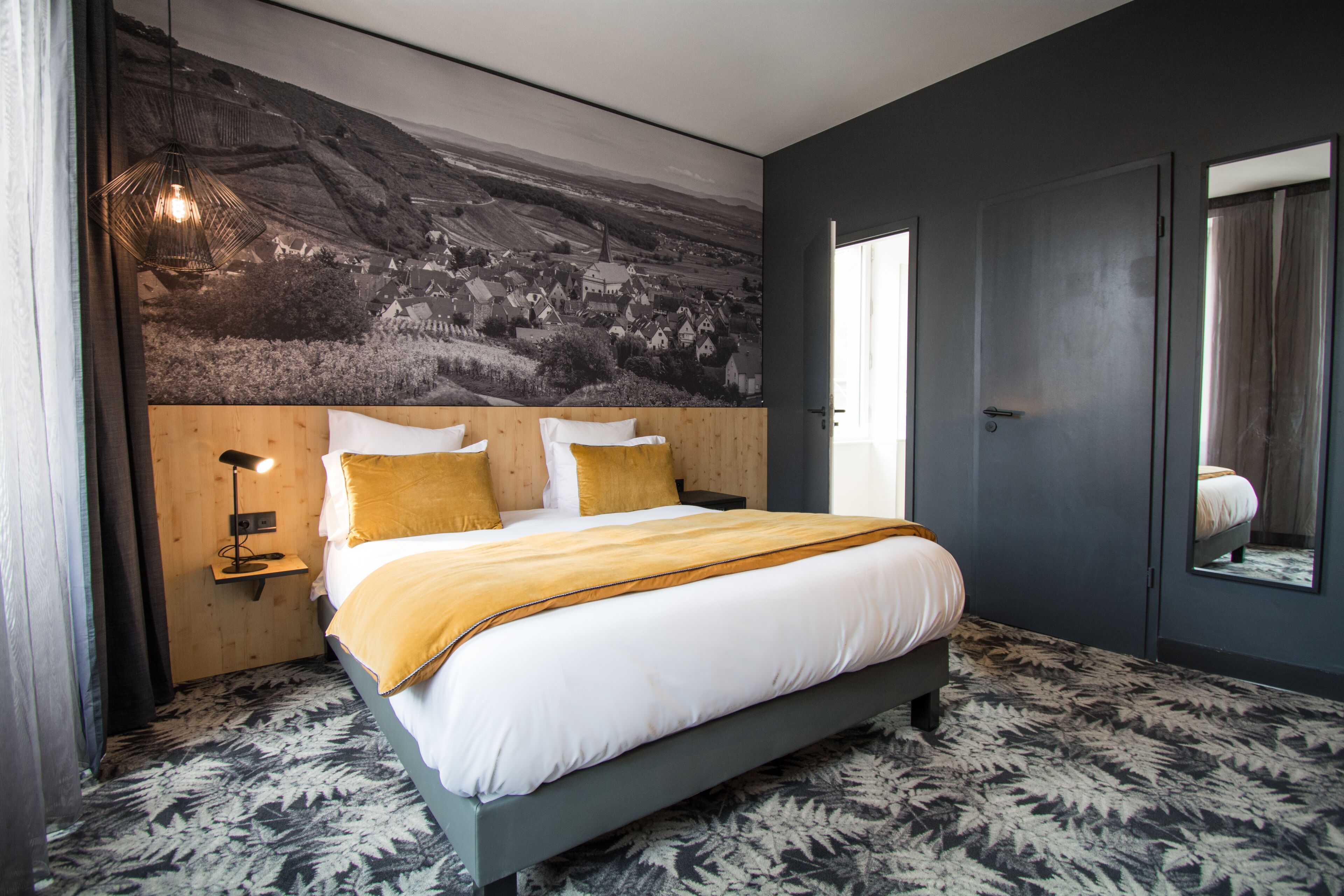 Un dormitorio moderno con una cama grande, un cabecero con un mural, una lámpara de noche y una alfombra estampada.
