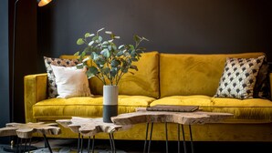 A yellow sofa with patterned pillows, a wooden coffee table, and a floor lamp. - L'Hôtel & Spa  Ribeauvillé (Ribeauvillé)