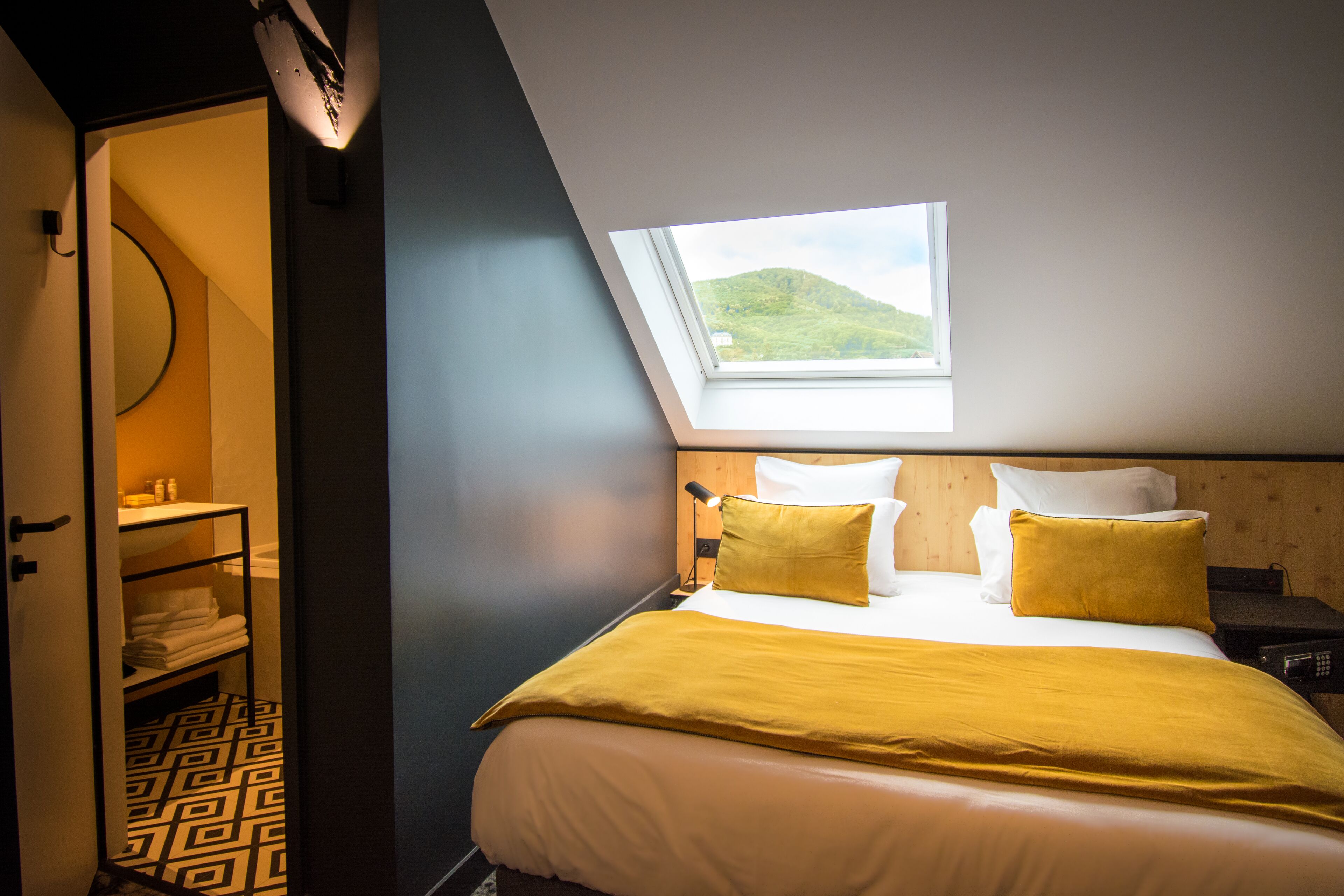 Un dormitorio con tragaluz, una cama con ropa de cama amarilla, una mesita de noche y una mesilla.