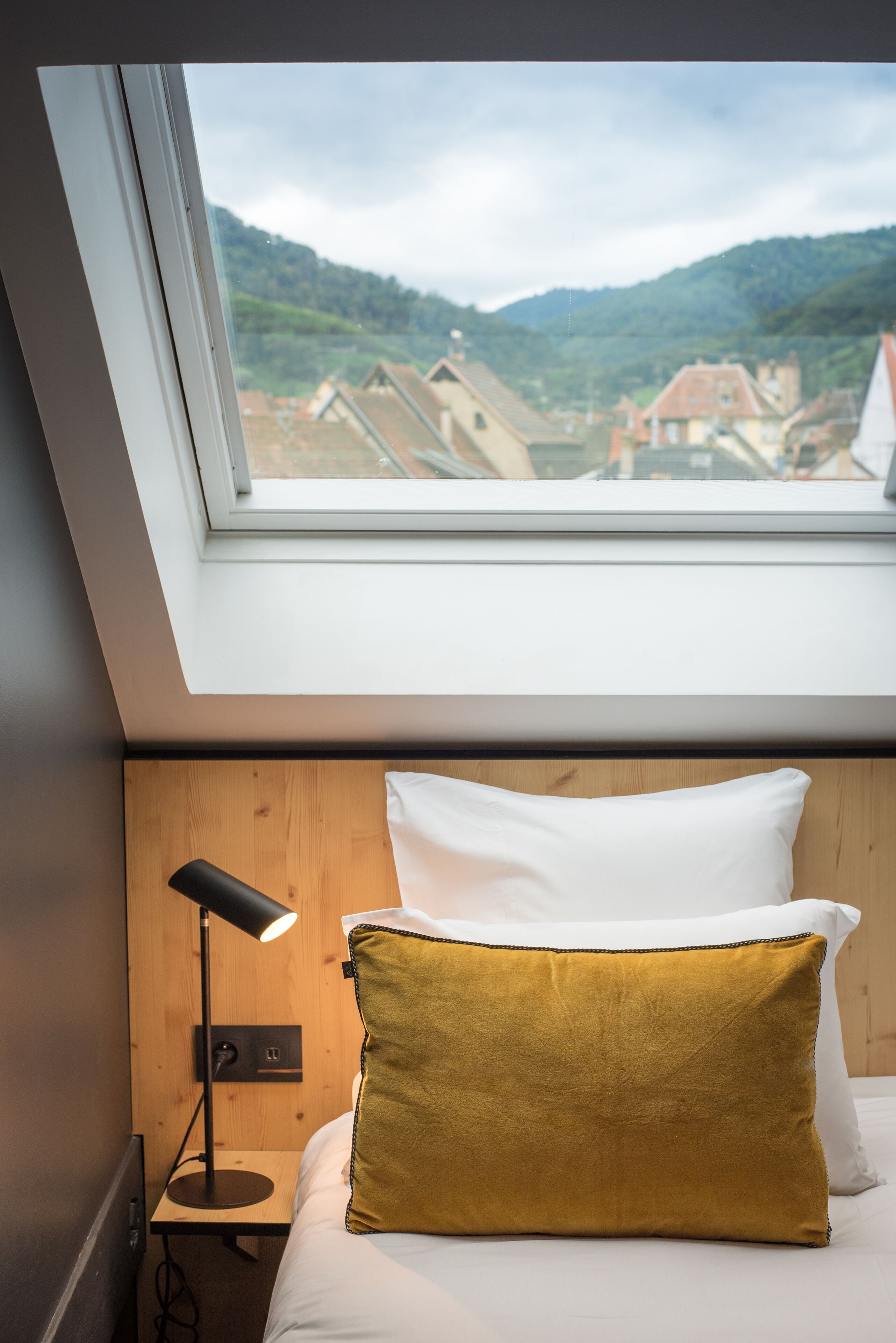 A bedroom with a skylight, a bed with white and mustard pillows, and a bedside lamp.