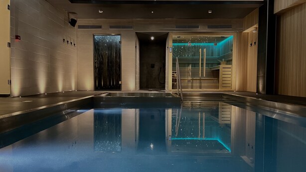 A modern indoor swimming pool with a clear water surface, a wooden reception area, and a wall with a vertical garden. - L'Hôtel & Spa  Ribeauvillé (Ribeauvillé)