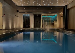 Une piscine intérieure moderne, dotée d’une eau cristalline, d’un espace d’accueil en bois et d’un mur agrémenté d’un jardin vertical.