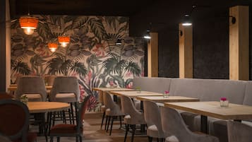 Un restaurant amb un mural tropical, taules de fusta i cadires amb coixins.
