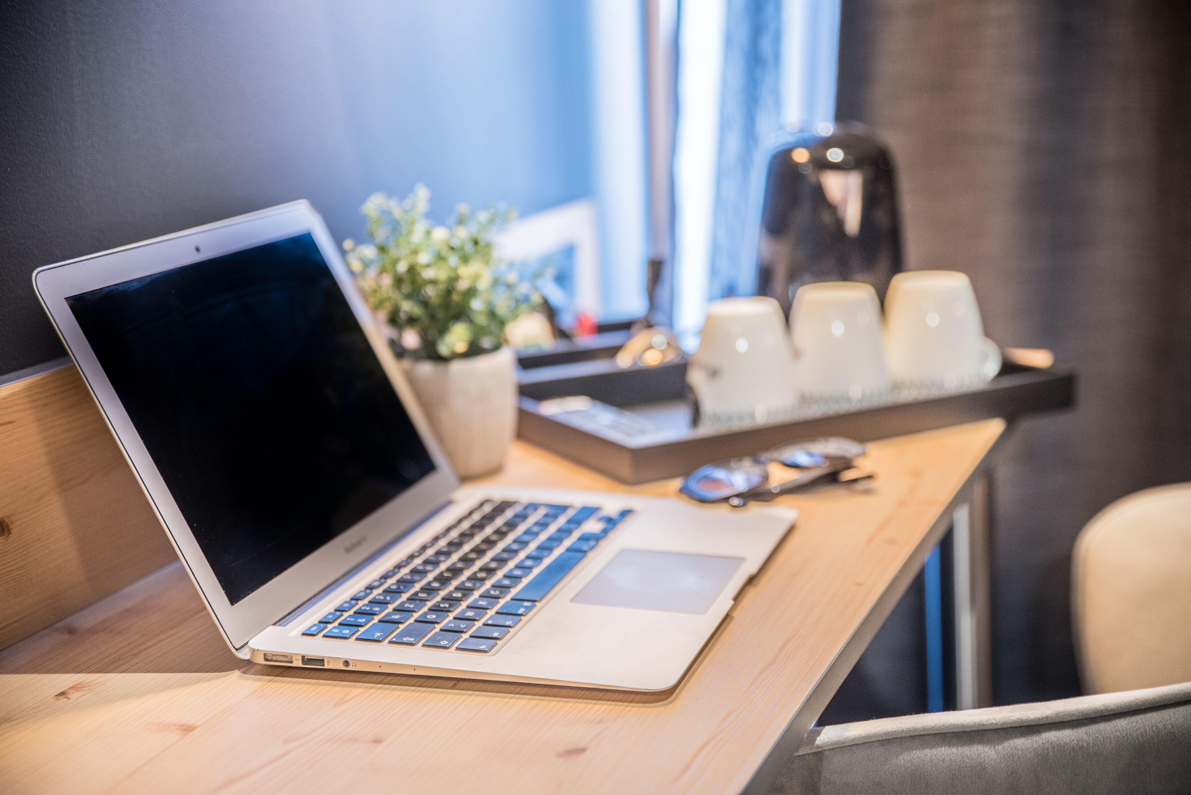 Un ordinateur portable est posé sur un bureau en bois, à côté d’une plante en pot et d’un plateau rempli de tasses.