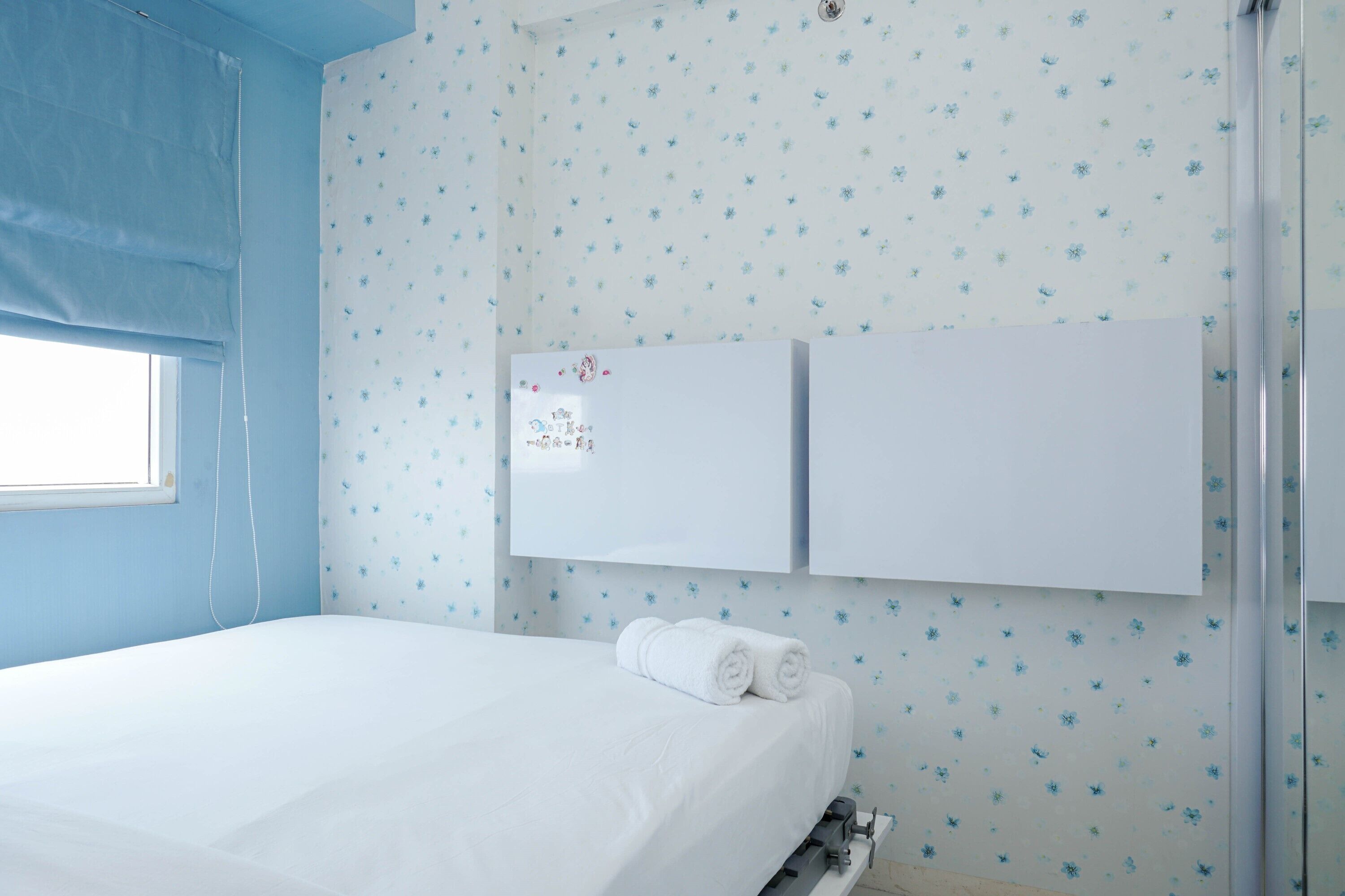 Un dormitorio con una cama, dos armarios blancos y un ventanal con cortinas azules.