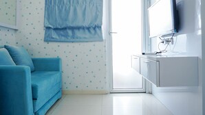 Una habitación con un sofá azul, un armario blanco con un televisor de pantalla plana y una ventana con cortina azul.