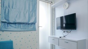 Una habitación moderna con una televisión montada en la pared, un armario blanco y una silla azul.