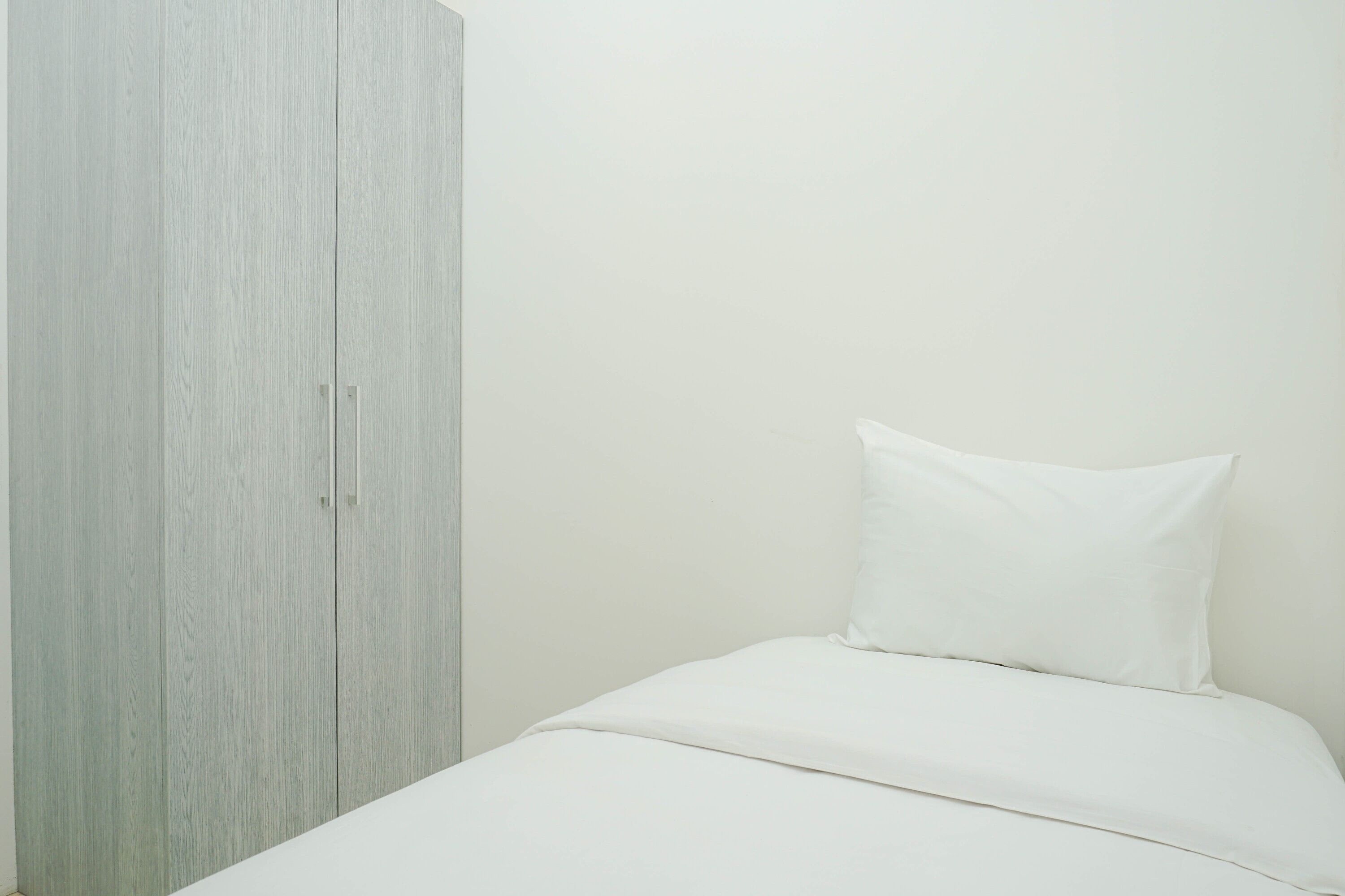 Un dormitorio con una cama, un almohadón blanco y un armario de tono claro.