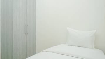 Un dormitorio con una cama, un almohadón blanco y un armario de tono claro.