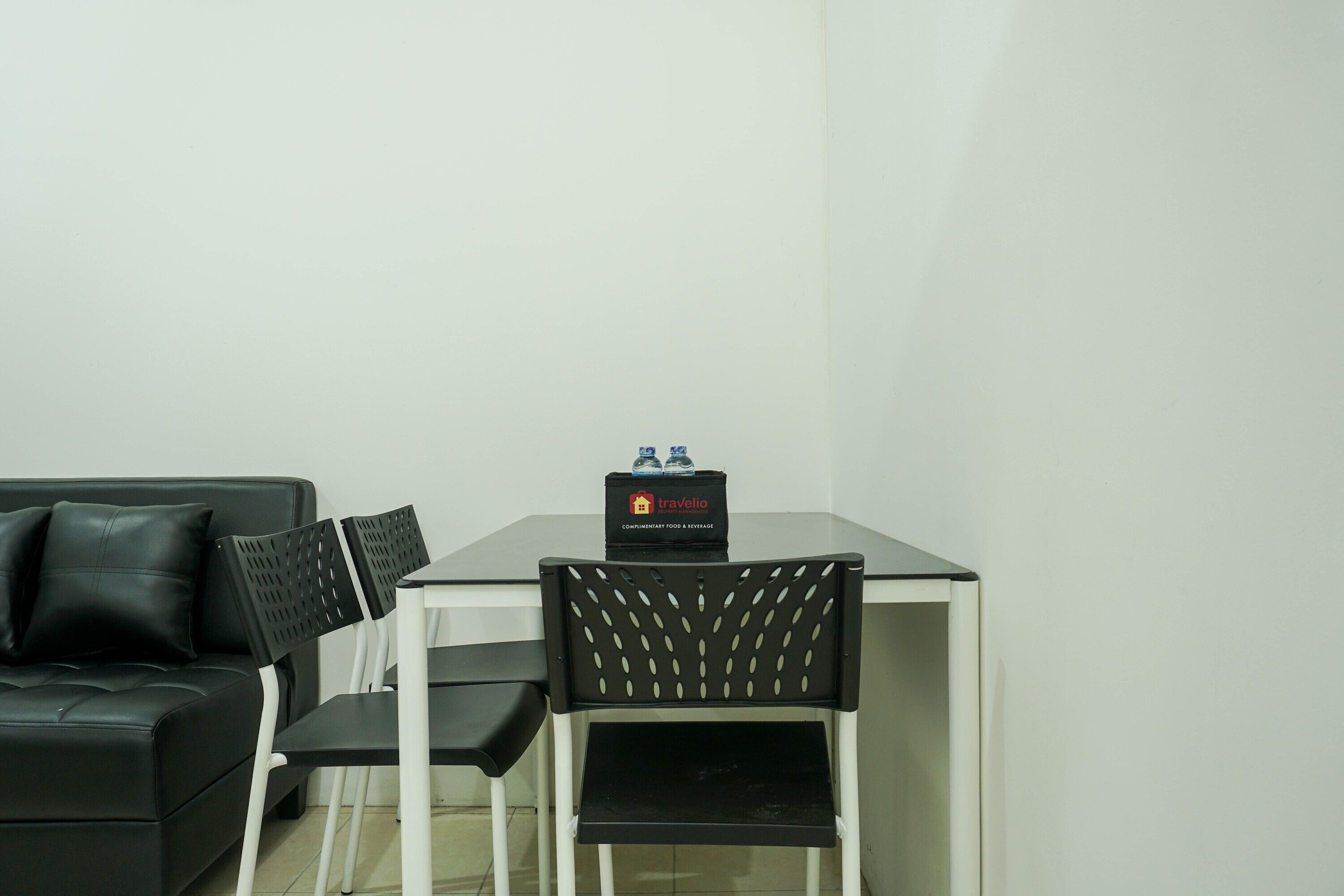 A small, modern room with a black leather sofa, a white table, and black chairs. A travel luggage box is on the table.