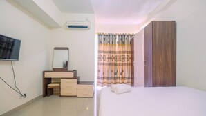 A hotel room with a bed, a TV, a desk with a mirror, a wardrobe, and a curtain. - Cozy Living Studio Apartment Taman Melati near Universitas Indonesia (Depok)