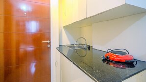 A kitchen with a black countertop, a red appliance, and white cabinets. - Cozy Living Studio Apartment Taman Melati near Universitas Indonesia (Depok)