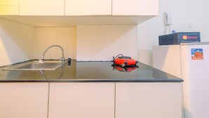 A kitchen with a black countertop, a stainless steel sink, and a red portable heater. - Cozy Living Studio Apartment Taman Melati near Universitas Indonesia (Depok)