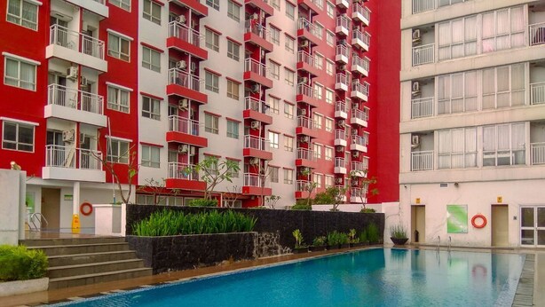 A swimming pool with a red and white building in the background. - Cozy Living Studio Apartment Taman Melati near Universitas Indonesia (Depok)