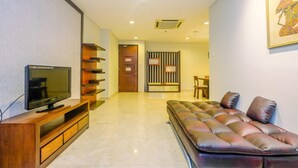 Una sala de estar moderna con un televisor de pantalla plana sobre un soporte de madera, un sofá capitonado con cojines, un separador a rayas y una puerta al fondo.