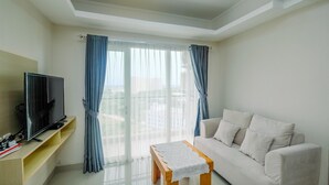 Ein modernes Wohnzimmer mit Flachbildfernseher, einer Couch, einem Couchtisch und einem Balkon mit blauen Vorhängen.