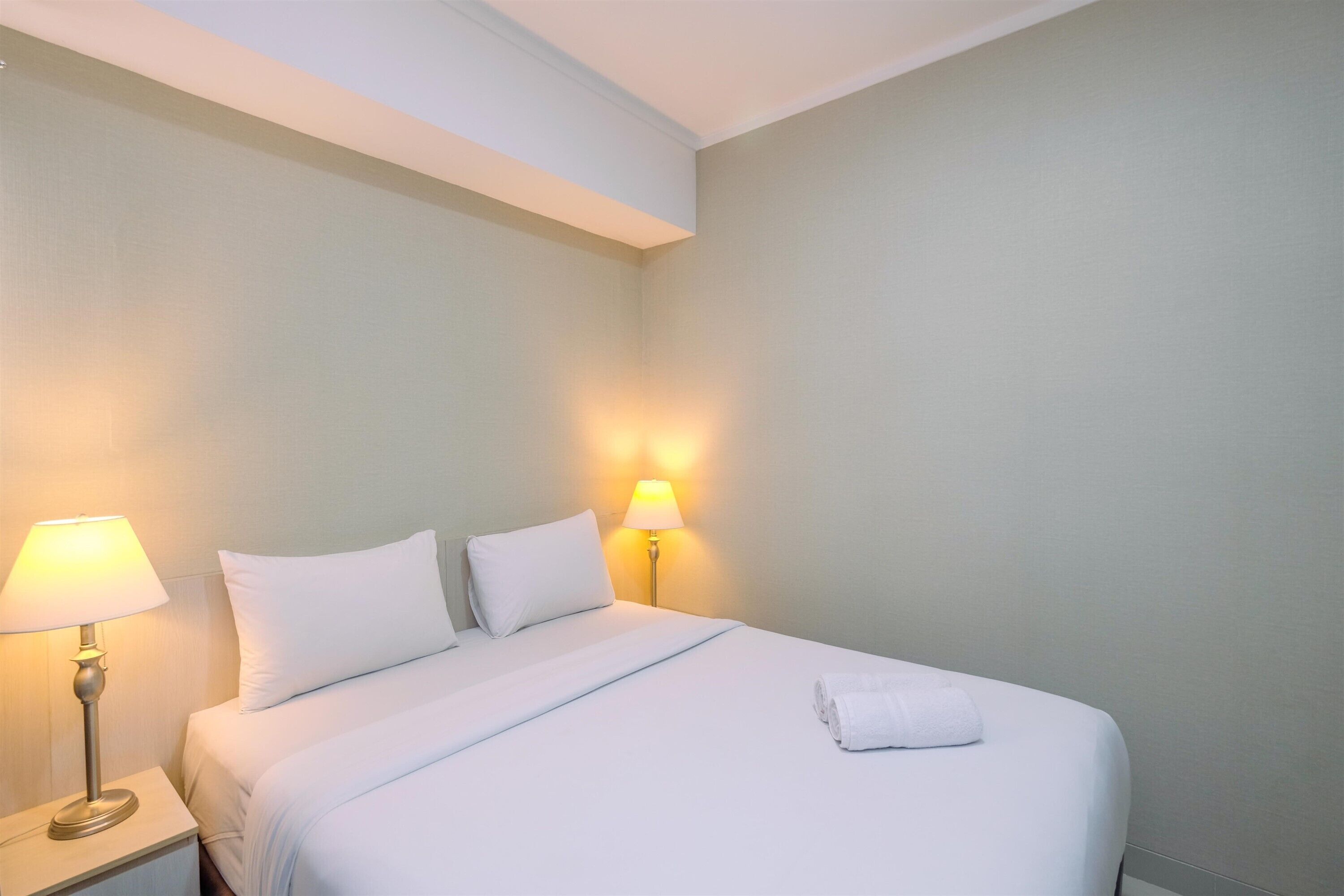 Un letto rifatto con lenzuola bianche, due abat-jour e un asciugamano piegato sul letto.