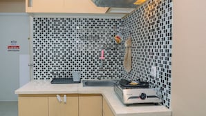 A kitchen with a checkered backsplash, a sink, a stove, and a cabinet. - Furnished Green Pramuka City 2BR Apartment near Mall (Jakarta)