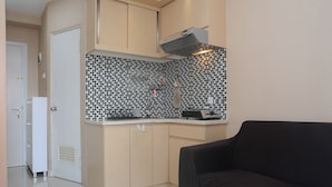 A compact kitchen with a tiled backsplash, a built-in oven, and a black countertop. - Furnished Green Pramuka City 2BR Apartment near Mall (Jakarta)