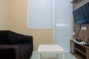 A room with a black sofa, a white table, and a TV mounted on the wall. - Furnished Green Pramuka City 2BR Apartment near Mall (Jakarta)