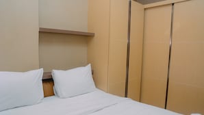 A hotel room with a bed, white bedding, a wooden headboard, and a wardrobe with sliding doors. - Furnished Green Pramuka City 2BR Apartment near Mall (Jakarta)
