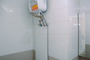 A bathroom with white tiled walls, a shower with a handheld showerhead, and a water heater with a 'SAVEWATER' label. - Furnished Green Pramuka City 2BR Apartment near Mall (Jakarta)