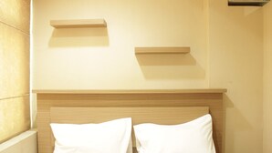 Une chambre d’hôtel avec une tête de lit en bois, deux oreillers blancs et deux étagères fixées au mur.