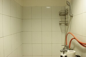 A bathroom with white tiled walls, a shower with a metal rack, and a toilet paper holder with rolls. - Well Appointed & Stylish 2BR at Jarrdin Cihampelas Apartment (Bandung)