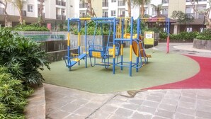 Un espace de jeux extérieur doté de structures d’escalade et de toboggans, entouré d’une piscine et de verdure.