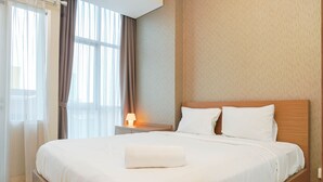 A neatly made bed in a hotel room with a wooden headboard, a bedside table with a lamp, and sheer curtains on the window. - Relax Studio Apartment at Capitol Park Residence (Jakarta)