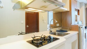 A modern kitchen with a gas stove, stainless steel sink, and wooden cabinets. - Relax Studio Apartment at Capitol Park Residence (Jakarta)