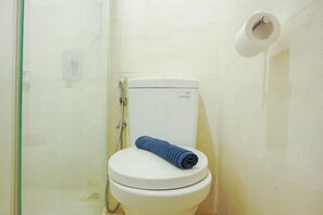 Des toilettes blanches avec une serviette bleue posée sur le couvercle, un porte-serviettes en papier et une paroi de douche en verre.