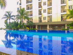 A hotel with a swimming pool surrounded by lush greenery and palm trees. - Best Deal and Cozy Studio Cinere Resort Apartment (Depok)