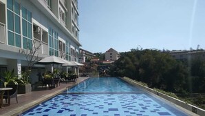 A swimming pool with a tiled pattern, surrounded by a building with balconies and outdoor seating.