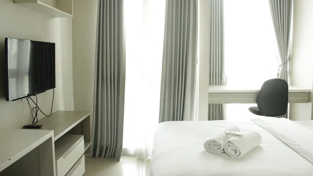 A hotel room with a bed, a TV, a desk, and curtains.