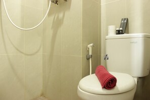 A bathroom with a toilet, a shower, and a toilet paper holder with a roll of toilet paper and a bottle on top. - Comfy Studio Apartment near UNPAD @ Taman Melati Jatinangor (Hegarmanah)