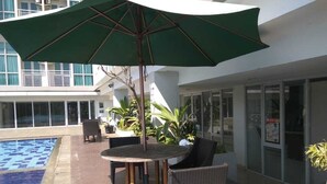 A poolside area with a round table, chairs, and a large umbrella.