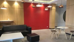 A modern lobby with a red accent wall, black leather seating, a white coffee table, and a round table with four chairs.