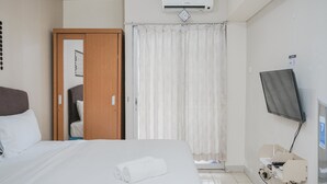 Ein Hotelzimmer mit Bett, Fernseher, Klimaanlage, Kleiderschrank und Vorhang.