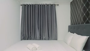 A neatly made bed with white linens and two rolled towels, a grey curtain, and a patterned wall. - Bassura City 2BR Apartment with Minimalist Design near Shopping Mall (Jakarta)